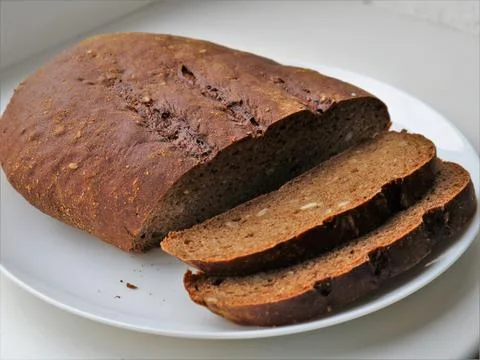Partially sliced loaf of rye bread on a white plate Stock Photos