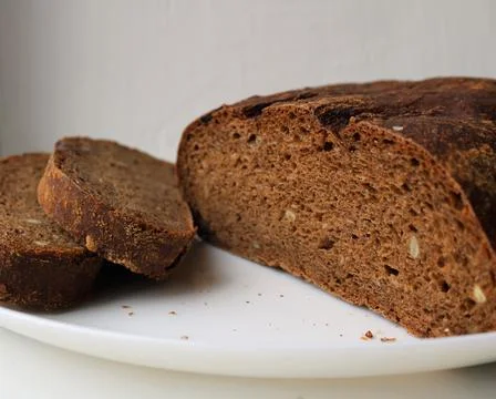 Partially sliced rye grain bread on a white plate Stock Photos