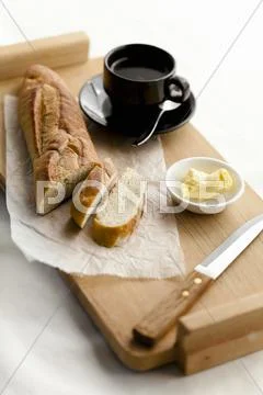 Partially Slices Baguette with Butter and a Cup of Coffee Stock Photos