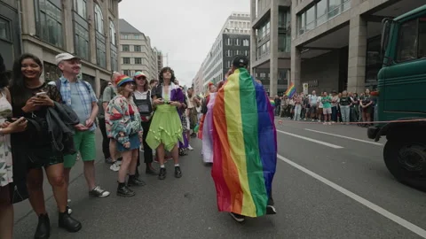 Participant wrapped in a large rainbow flag marches along a central Berlin Stock Footage 346240619