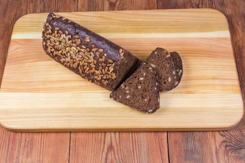 Partly sliced brown bread triangular shape on wooden cutting board 스톡 사진