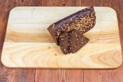Partly sliced brown bread triangular shape on wooden cutting board Foto stock
