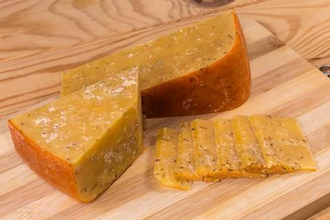 Partly sliced hard cheese with adding cumin on cutting board Stock Photos