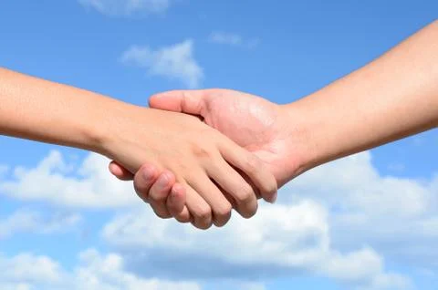 Partner hand between a man and a woman on blue sky background, teamwork Stock Photos