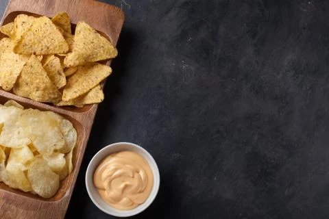 Party snack, chips, Nacho with cheese sauce in a wooden plate on the dark con Stock Photos