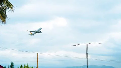 Passenger airplane taking off into a cloudy sky above city infrastructure. Stock Photos