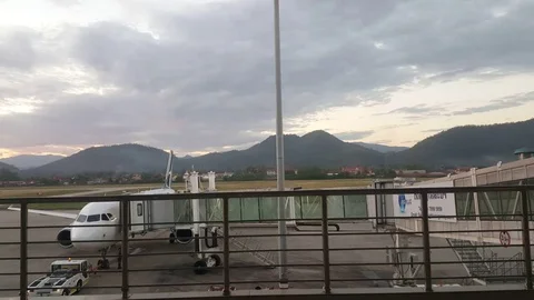 Passenger boarding bridge extends, plane, Luang Prabang Airport, hills, fence Видео 77783459