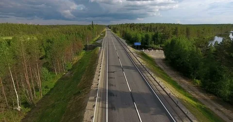 Passenger bus driving in evergreen forest on asphalt road across river. Russia Vidéo 77697796
