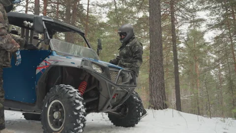 Passenger climbs into blue atv driver secures harness engine revs on snowy pine Stock Footage 332055701