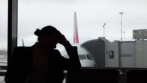 Passenger disappointed by flight delay, silhouetted view against airliner Stock-Footage 77062754