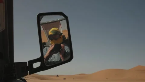 Passenger in goggles reflected in buggy side mirror on Sahara dunes Stock Footage 344584290