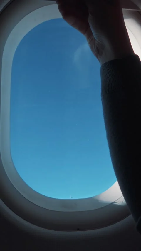 Passenger hand reaching for airplane window, revealing clear blue sky outside, 库存影片 329201797