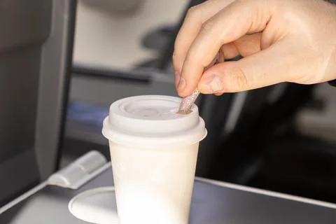 A passenger inserts a straw into a disposable paper cup on an airplane tray.. Stock Photos
