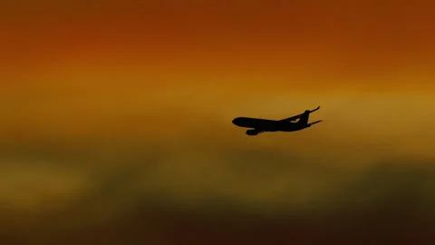 Passenger jet silhouette flying through orange sunset clouds Stock Footage 341016337