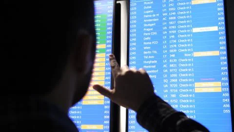 Passenger looking at timetable screen board and pointing with a finger searching Foto stock