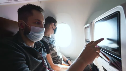 Passenger with masked faces using seatback monitor screen for entertainment. Stock Footage 165259347