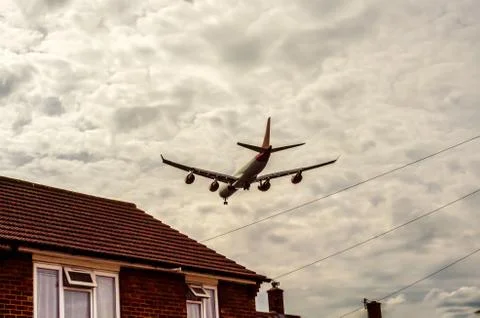 Passenger plane flying over the roofs of residential homes, low airplane flie Stock Photos