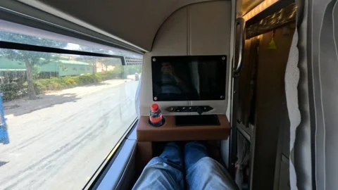A passenger in sleeper bus, upper bunk with TV. Legs. Street view from a window Stock Footage 248679300