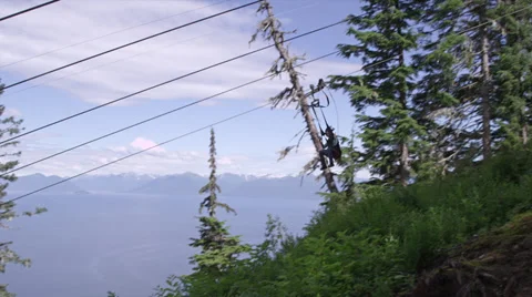 A passenger takes a ride down a zip line overlooking the ocean in Alaska Stock Footage 35064936
