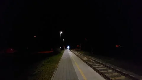 Passenger train approaching a rural railway station platform at night with brigh 库存影片 335474963