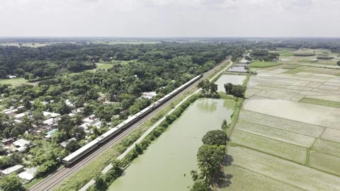 Passenger train crossing green fields beside ponds above Stock Footage 344544211