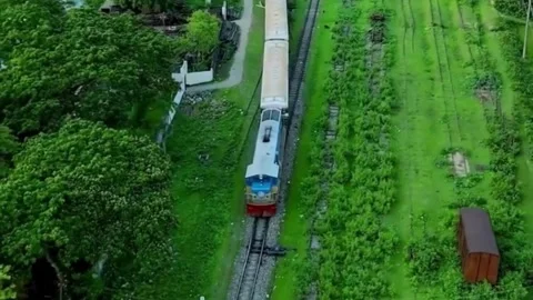 A passenger train cuts through a vibrant, lush green landscape and forest Stockbeeldmateriaal 336703030