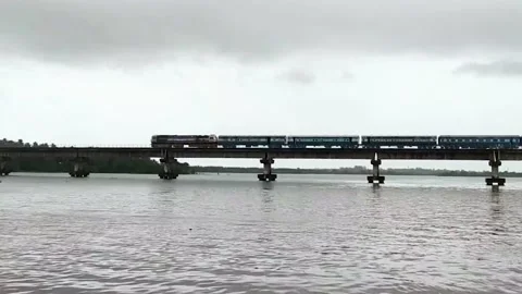 Passenger train moving across the river on the bridge on a cloudy day in Indi Stock Footage 133941628