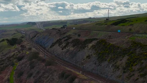 Passenger train moving in distance and road with cars driving along cliff Stock Footage 306537311