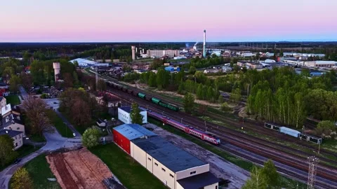 Passenger train passing parked at industrial town with a cargo train at sunset Stock Footage 340282016