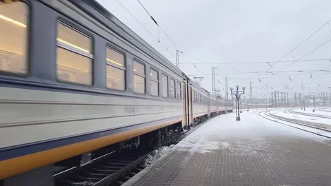 A passenger train pulls up to the platform of the railway station. There is snow Stock Footage 267131502