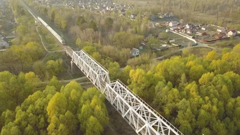Passenger train rides through the forest and the bridge over the river. Video stock 107083825