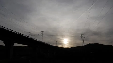Passenger Train Silhouetted on Elevated Bridge at Sunset with Power Lines in Stock Footage 337694470
