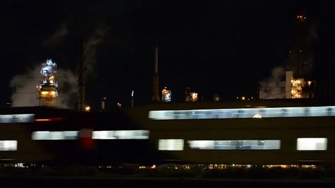 Passenger Train Speeding Past Oil Refinery at Night - HiFi Stereo Audio Stock Footage
