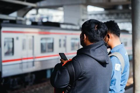 Passenger using cell phone were standing waiting for the arrival of the commuter Stock Photos