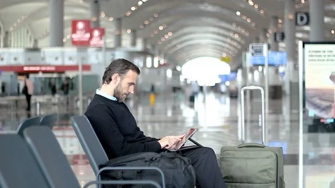 Passenger using his tablet waiting at departure lounge at the airport Stock Footage 99069068