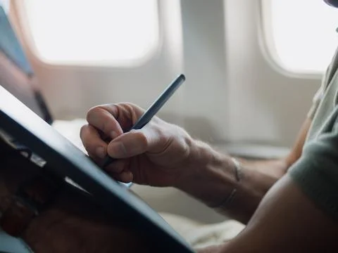 Passenger using stylus on tablet during airplane flight Stock Photos