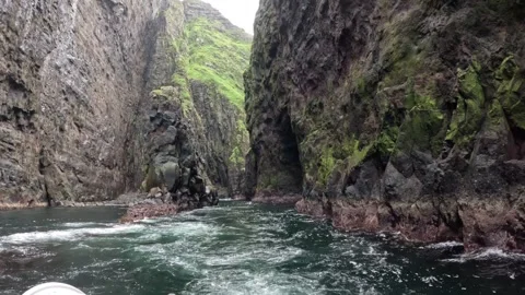 Passenger vessel sailing close to towering volcanic cliffs and rock formations Stock Footage 339318710