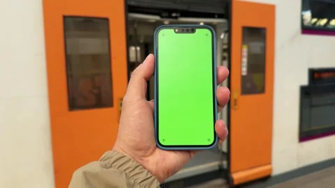 Passenger walking and holding mobile phone with green screen on station platform Stock Footage 286098313
