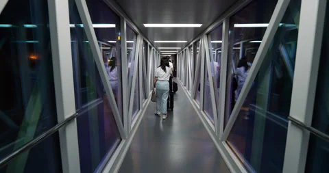 Passenger walking through boarding bridge jetway to terminal at night Stock Footage 320117630