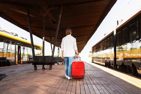 Passenger is walking on a train station platform. The man pulls a red suitc.. Stock Photos