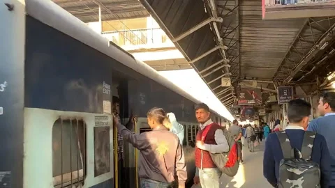 Passengers board blue train on sunlit platform in India Stock Footage 306780506