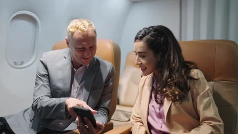 Passengers businessman using smartphone talking with women colleague in airplane Stock Footage 242386932