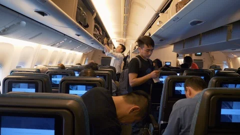 Passengers Inside the Plane Look for Seats, Put Away Things, Sit Down in Chairs Stock Footage 122989865