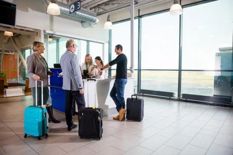 Passengers With Luggage Standing While Receptionists Working At Stock Photos