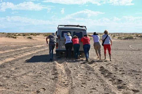 Passengers pushing a van stuck in the sand Stock Photos