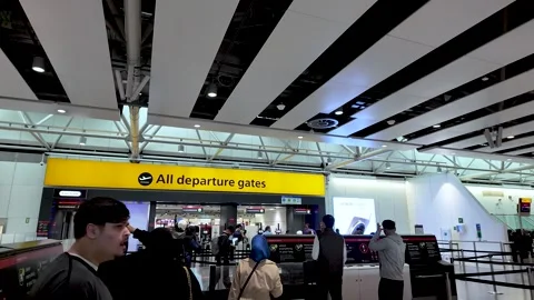 Passengers queue at Heathrow airport beneath a bright 'All departure gates' Stock Footage 334973319
