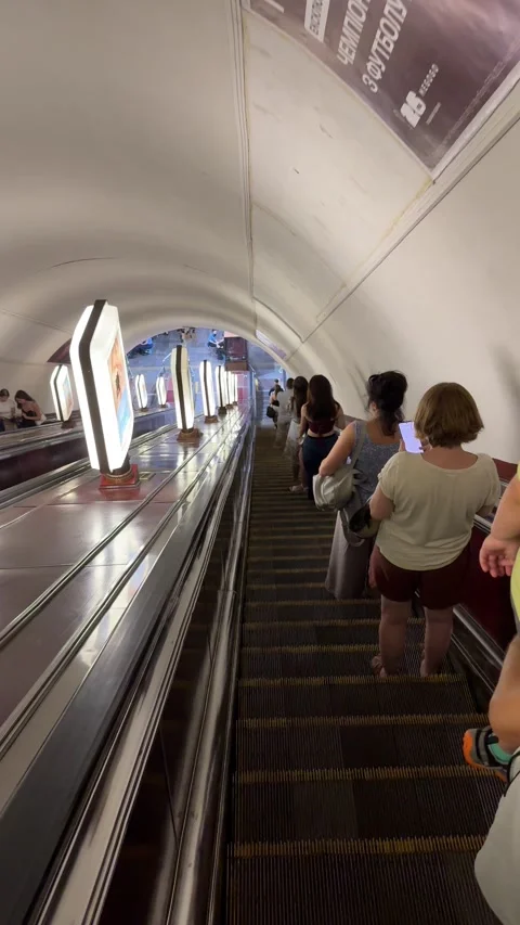 Passengers riding down a long escalator during rush hour in Kyiv metro Stock Footage 340324534