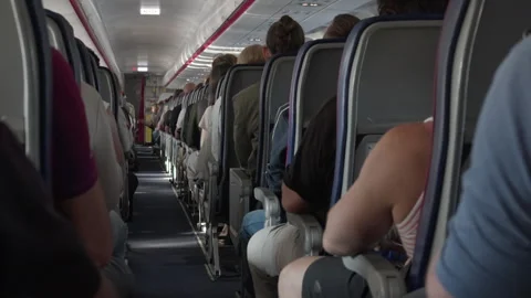 Passengers sit in crowded economy class seats inside airplane cabin on flight Stock Footage 343950393
