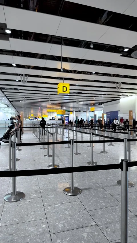 Passengers stand in stanchion-lined check-in queues beneath bright yellow Stock Footage 334973334