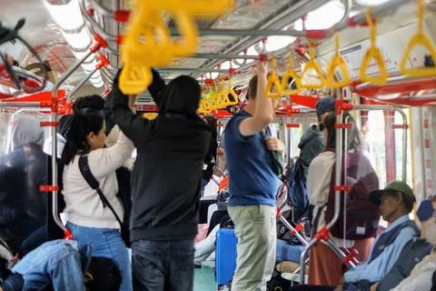 Passengers stand while holding yellow handrails in a crowded commuter electric Stock Photos